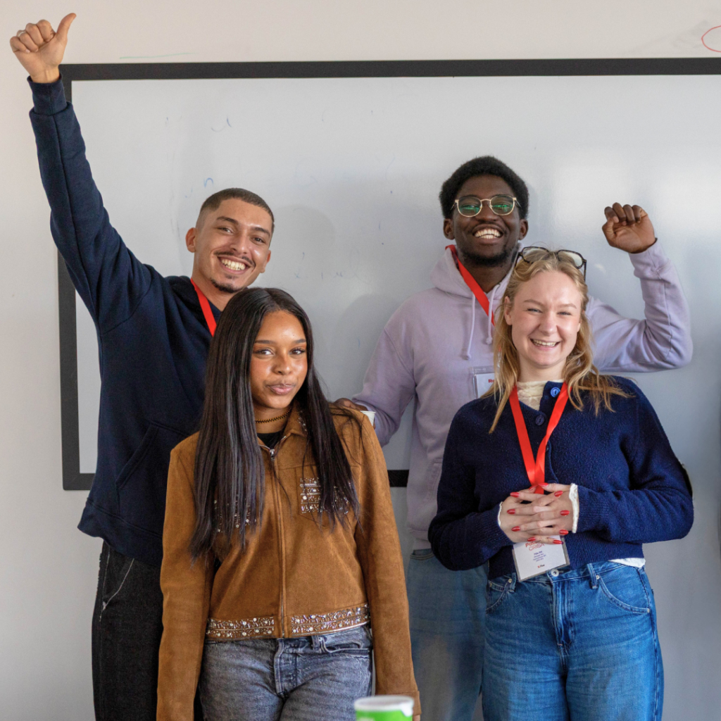 Quatre jeunes adultes souriants devant un tableau blanc