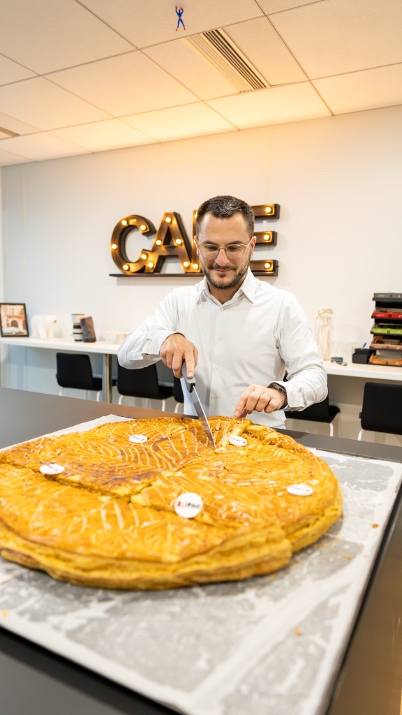 Homme découpant une grande galette dans un bureau.