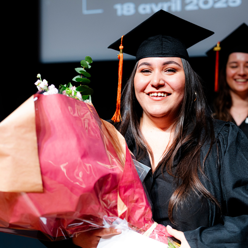 Étudiante diplômée avec bouquet et toge noire.
