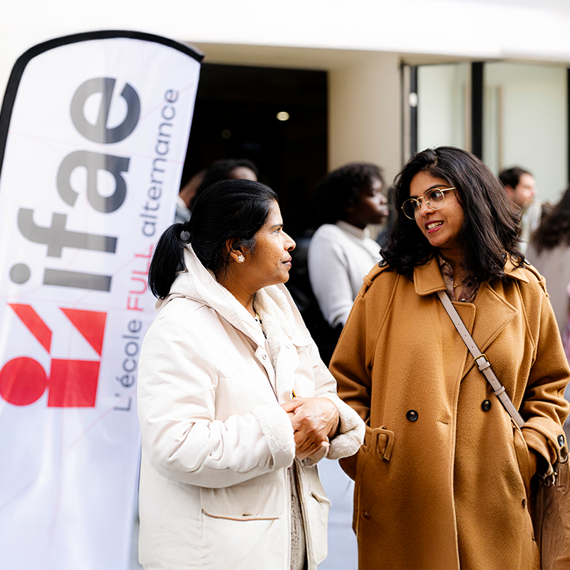 Deux femmes discutent devant un drapeau IFAE.
